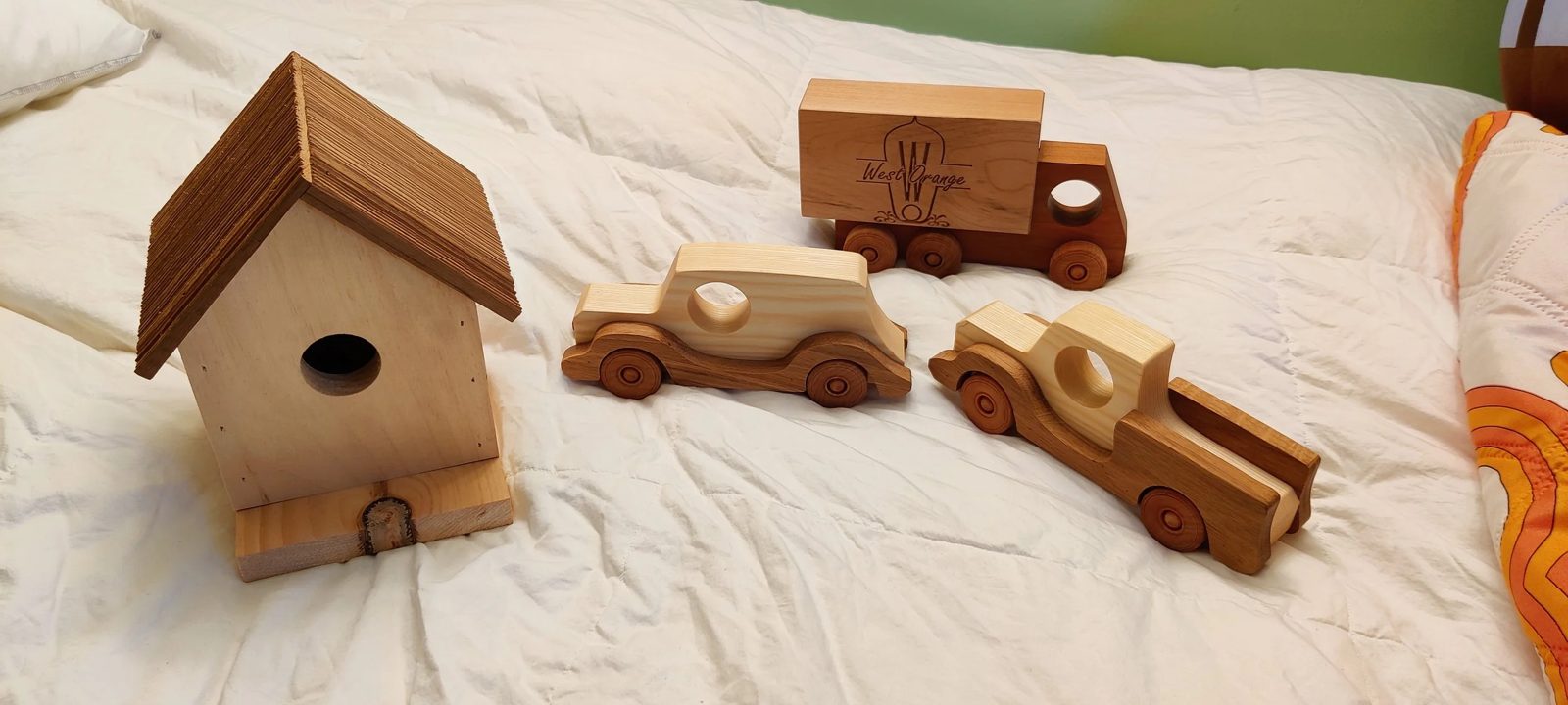 Wooden toy cars and a box truck beside a cedar-roofed birdhouse