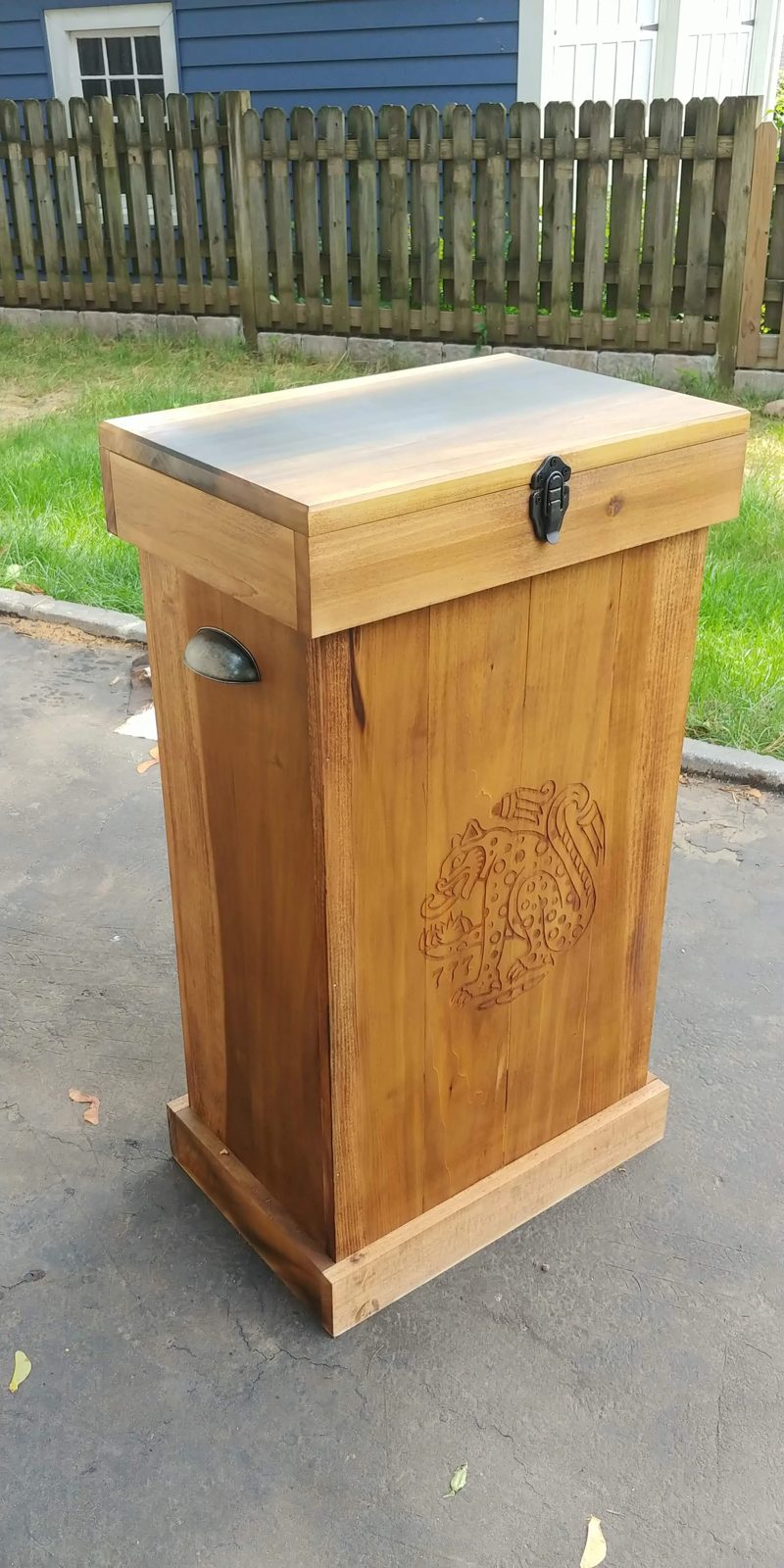 A tall lidded wooden storage chest with a carved jaguar panel and cast-iron hardware